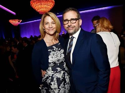 Steve Carell is wearing a blue suit and Nancy Carell is wearing a dress with flowers designed on it.